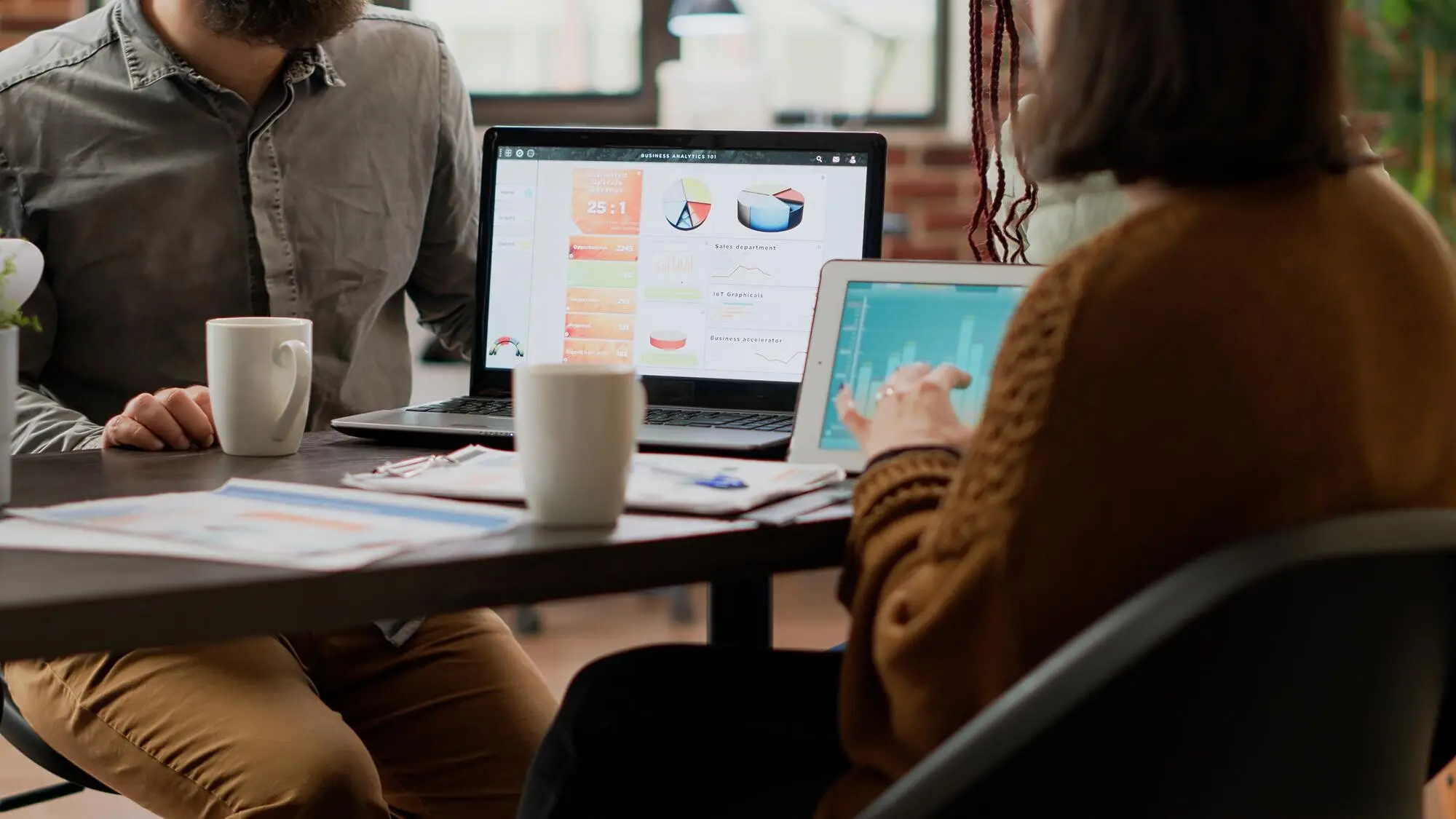 Eine multiethnische Gruppe von Kollegen arbeitet mit einem digitalen Tablet an der Analyse von Diagrammen und nutzt Informationen aus Online-Recherchen, um einen Infografikbericht zu erstellen. Personen analysieren Diagramme im Sitzungssaal, praxisnah und nachvollziehbar.